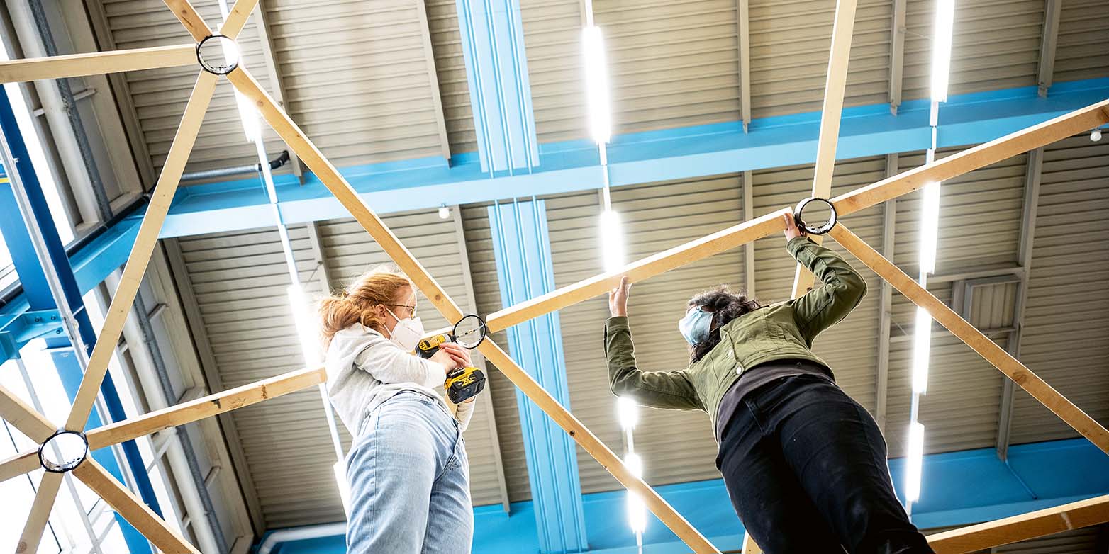 Zwei Frauen mit Schutzmasken halten Holzteile der Kuppel in die Höhe