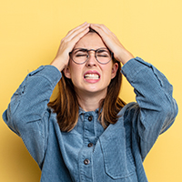 A woman grabs her head and tensely contorts her face