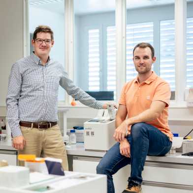 A small machine in a laboratory between Benedikt Wanner on the left and Guillaume Coin on the right.