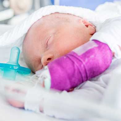 A sleeping baby in the intensive care unit. A pacifier lies next to the baby.